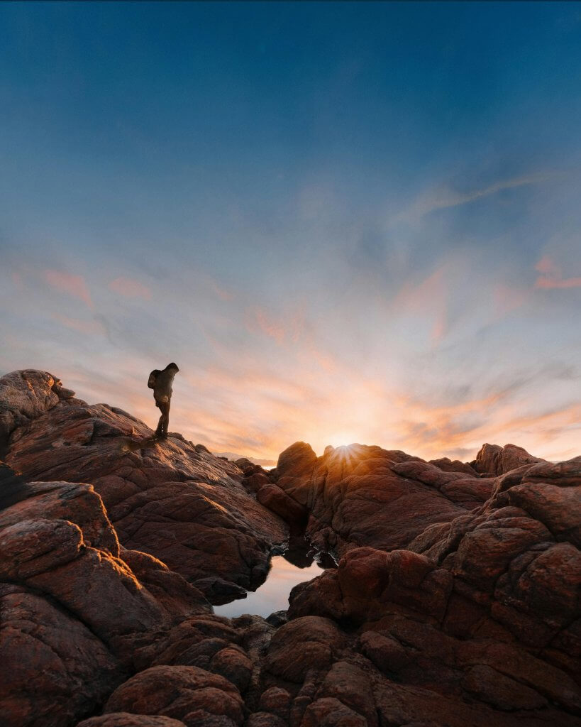 homme qui randonne sur des rochers et leve de soleil