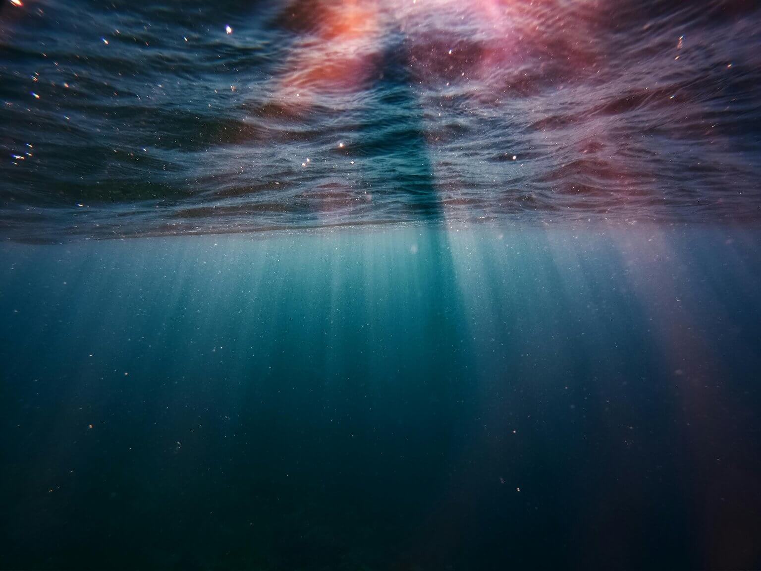 Vue sous la mer des rayons de lumières traversant l'eau sombre.